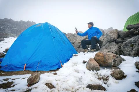 A man sitting in camping tent, using smartphone Stock Photos