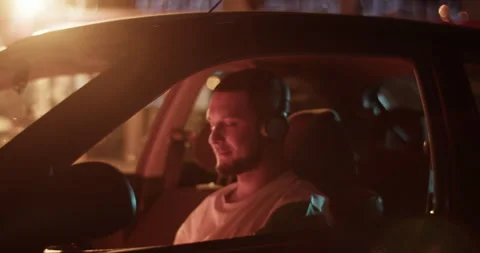 Man sitting in car and taking off headphones at night Stock Footage 244524947
