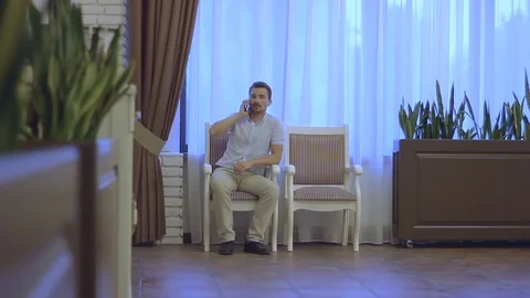 The man is sitting on a chair and talking on the phone Stock Footage 78614018