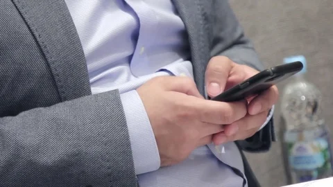 Man sitting on a chair in his jacket is typing something in the phone Stock Footage 76983786