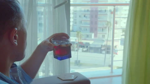 Man sitting in a chair, looking thoughtfully out the window and drinking Stock Footage 294300341
