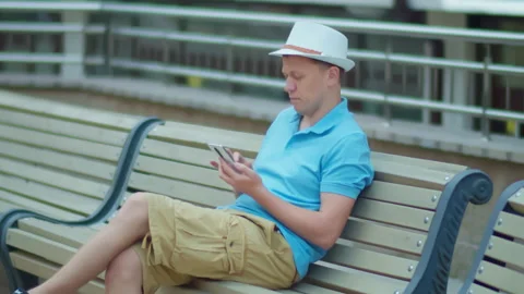 Man sitting on a city bench with a mobile phone in his hands, camera tracking Stock Footage 146865679
