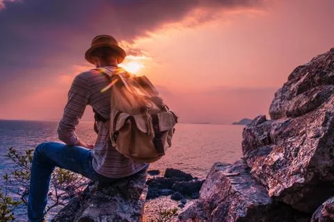 A man sitting on the cliff with backpack looking sea sunset view. concept Tra Stock Photos