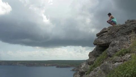 Man sitting on a cliff, huge clouds gathered over a land adjoining the sea Stock Footage 77803545