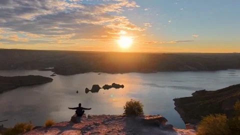 Man sitting on a cliff with open arms enjoying a spectacular sunset with hi.. Stock Footage 338019726