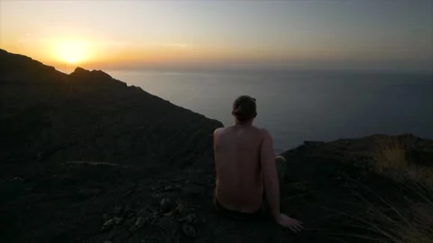 Man sitting on Cliff with Sunset and ocean in Horizon Vídeo Stock 135895358