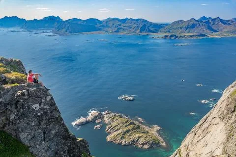 Man sitting on cliff top looking at rocky islands and clear sea water Stock Photos