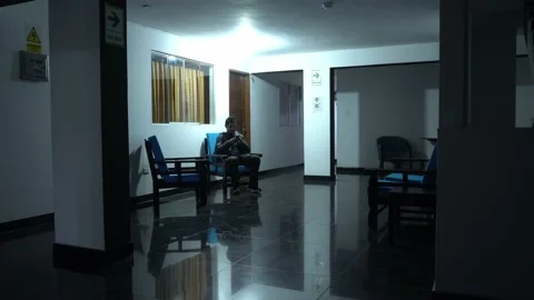 A man sitting in a common space in a hotel looking at his cell phone at night in Video stock 196738154