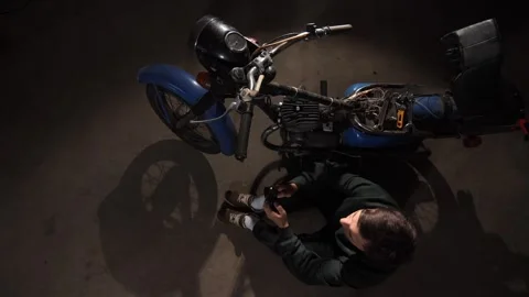 Man sitting on a concrete floor in a dimly lit garage, taking a work break from Stock Footage 342773562