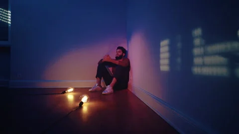 Man sitting in a corner smoking a cigarette with light bulbs on the floor Stock Footage 135386988