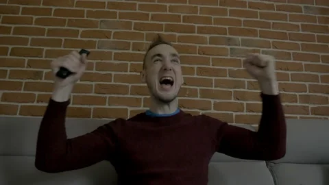 A man sitting on the couch and eagerly rejoices in the victory Stock Footage 130640708