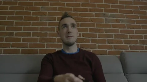 A man sitting on a couch and pointing at the TV with his remote control Stock Footage 130640955