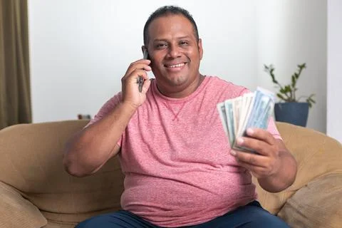 A man is sitting on a couch and talking on his cell phone Stock Photos