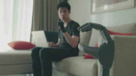 A man is sitting on a couch and using a laptop to develop Robot arm Stock Footage 314612166