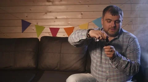 A man sitting on a couch and vaping e-cigarette. 4K UHD Vídeo Stock 63116588