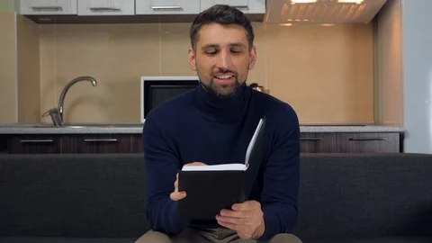 Man is sitting on the couch and writes tasks, goals, dreams, ideas in a notebook Stock Footage 121842353