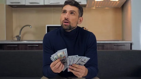 Man is sitting on the couch, counting a pack of money and plans his purchases Stock Footage 121842235