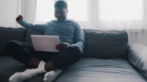 Man sitting on a couch cross-legged with a laptop in his lap Video stock 153879154