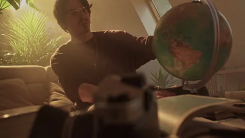 Man sitting on couch exploring a globe in a cozy living room Stock Footage 319963666