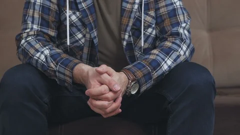 A man sitting on the couch gesticulates with his hands, crossing his palms. Stock Footage 103979045