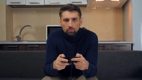 Man is sitting on the couch, hold gamepad, playing video game on console Stock Footage 121841947