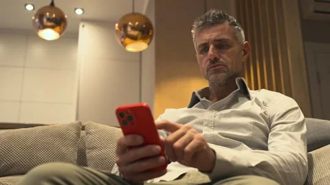 Man sitting on the couch holding his mobile phone in hands and scrolling. Stock Footage 299708790