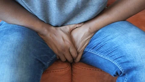 Man sitting on couch holding his groin area in pain or discomfort while wea.. Stock Footage 332625854