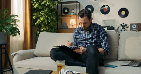 The man is sitting on couch at home doing homework for extra English classes Stock Footage 200816176