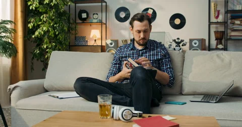 The man is sitting on couch at home doing homework for extra English classes Stock Footage 200819232