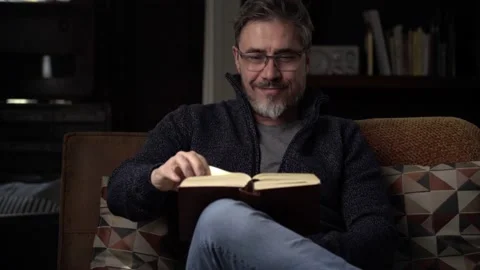 Man sitting on couch at home reading book Stock Footage 150214124