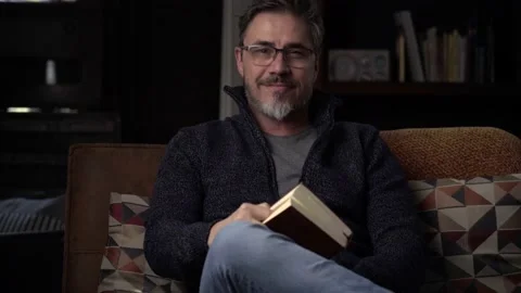 Man sitting on couch at home reading book Stock Footage 150214135