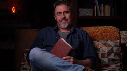 Man sitting on couch at home reading book Stock Footage 150214847