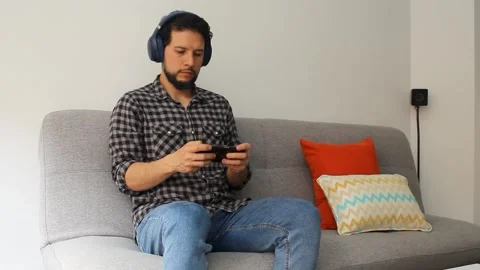 Man sitting on a couch playing games on his smartphone 库存影片 340583422