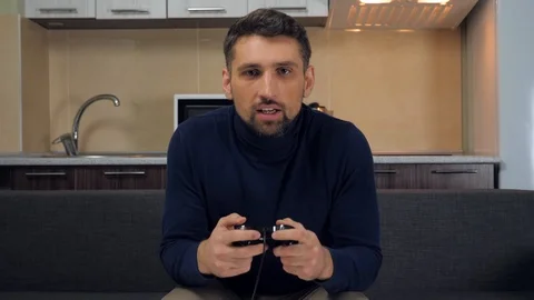 Man is sitting on the couch, playing video game on console, win and stands up Stock Footage 121841934