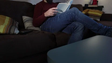 A man sitting on the couch relaxes reading a book Stock Footage 121157987