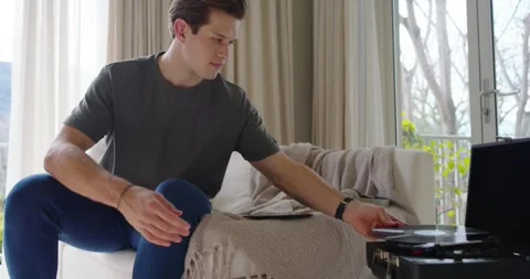 Man sitting on couch sorting vinyl, placing record on suitcase-turntable Stock Footage 347753206