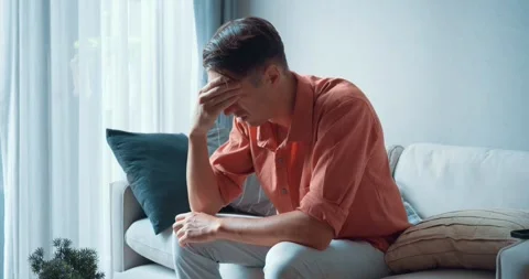 A man sitting on couch takes off his glasses, feeling headache. Fatigue takes Stock Footage 260467586