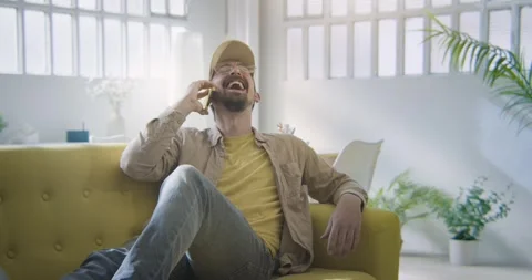 A man is sitting on a couch talking on a cell phone laughing Stock-Footage 270519128