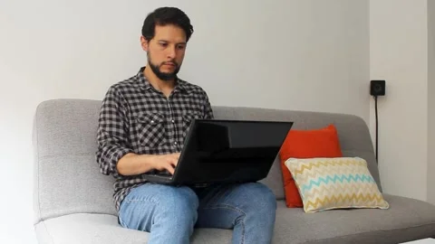 Man sitting on a couch typing on a laptop over his legs in a home office concept Vídeo Stock 340583467