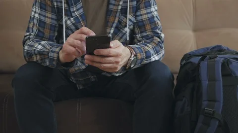 A man sitting on the couch uses the Internet in a smartphone, next to him is a 스톡 동영상 103938768