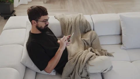 A man is sitting on a couch using a cell phone Stock Footage 265403993
