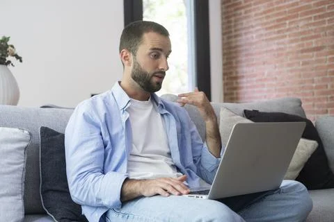 A man sitting on a couch using a laptop for a video call and remote work, g.. 写真素材