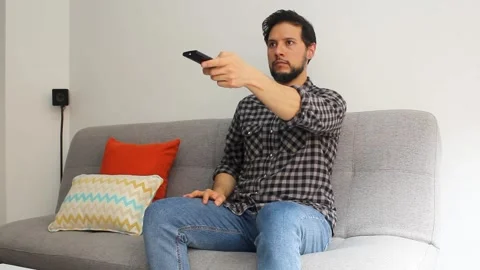 Man sitting on a couch using a remote controller of a smart tv Stock Footage 340583389