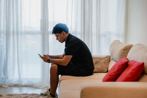 Man sitting on couch using smartphone in bright living room Stock Photos