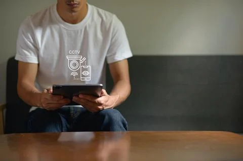 Man Sitting on Couch Using Tablet with Security Camera Icon Overlay, Casual.. Stock Photos