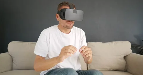 Man sitting on couch, using Virtual Reality headset, gesturing with fingers. Stock Footage 168493755