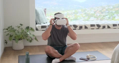 Man sitting cross-legged on mat, putting on white VR headset and headphones for Stock Footage 336958441