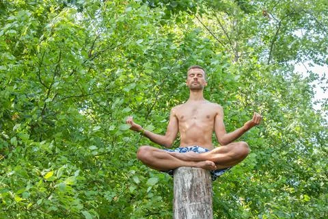 Man sitting on cut off trunk of tree and meditating with his hands turning up Stock Photos