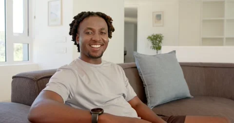 Man sitting on dark gray couch smiling then laughing as camera moving closer, Stock Footage 341393760