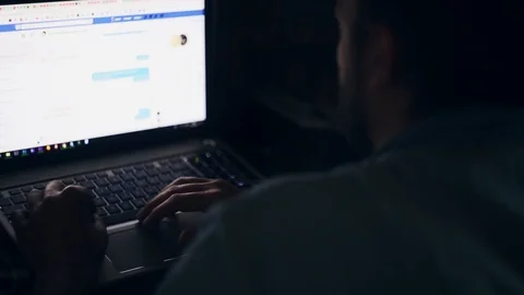 Man sitting at dark room, working with laptop view on screen from behind Stock Footage 108594996